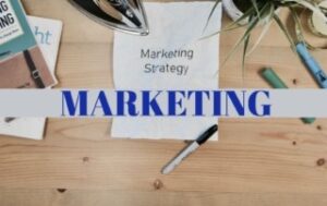 A desk with a piece of paper with the words Marketing Strategy typed on it with a band across the desk saying marketing